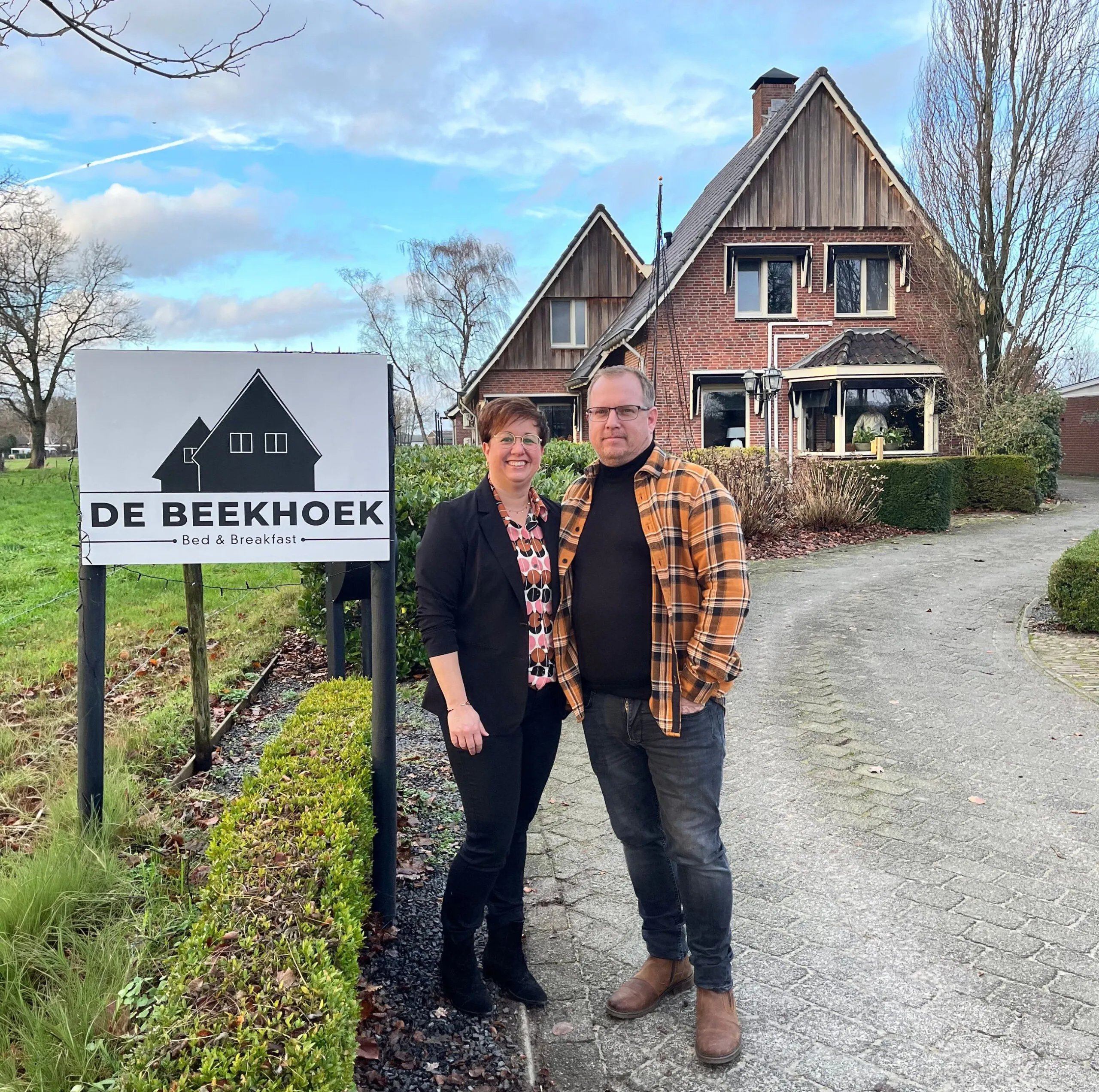 De eigenaren van B&B De Beekhoek bij het bord voor hun boerderij