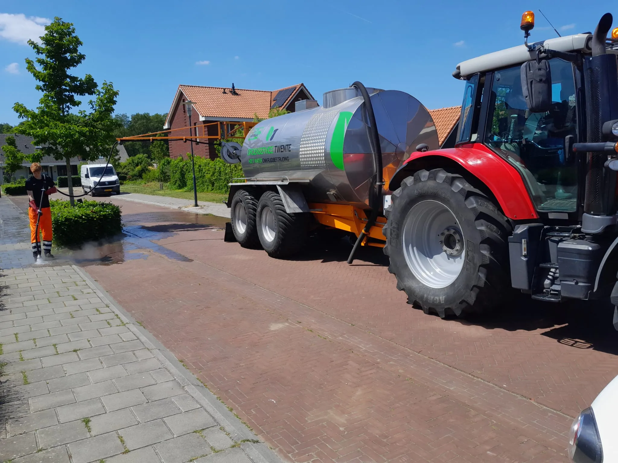 Een medewerker van Groenservice Twente reinigt de straat naast de tractor met tank